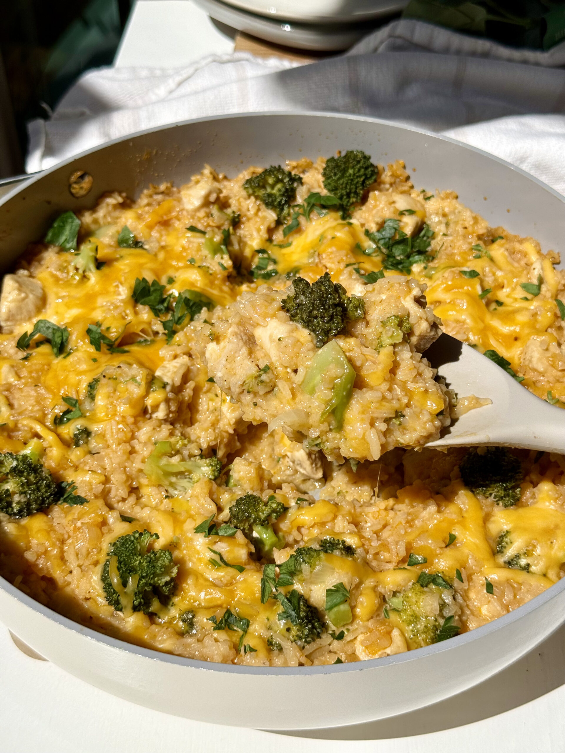 Healthy chicken broccoli rice casserole in a skillet with a spoon lifting up a portion.
