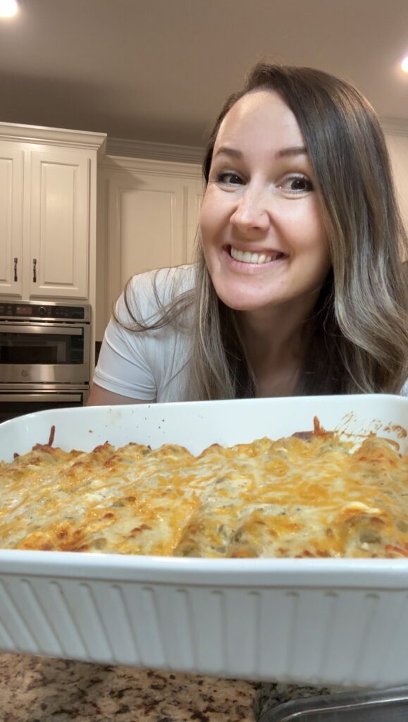 A woman holding up a pan of baked chicken enchiladas with sour cream.