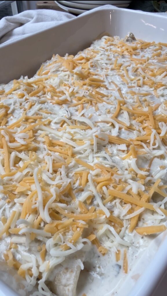 Adding the cheese over the top of the pan of chicken enchiladas.