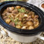 Crockpot steak bites and baby potatoes coated in savory beef gravy and garnished with fresh thyme