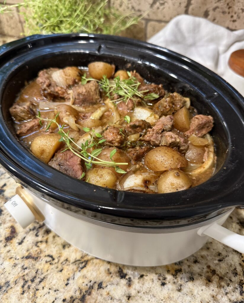 Crockpot steak bites and baby potatoes coated in savory beef gravy and garnished with fresh thyme