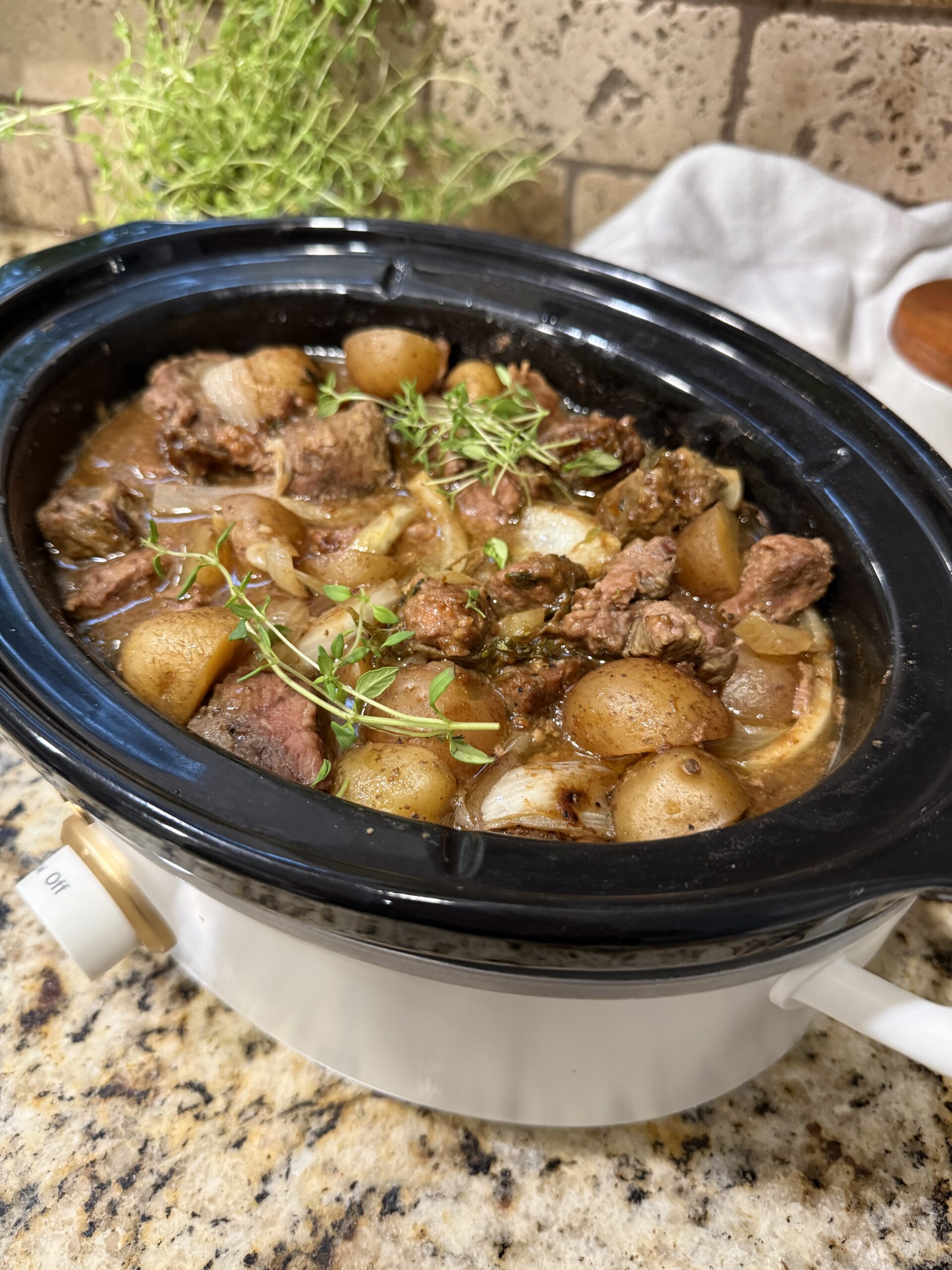 Crockpot steak bites and baby potatoes coated in savory beef gravy and garnished with fresh thyme