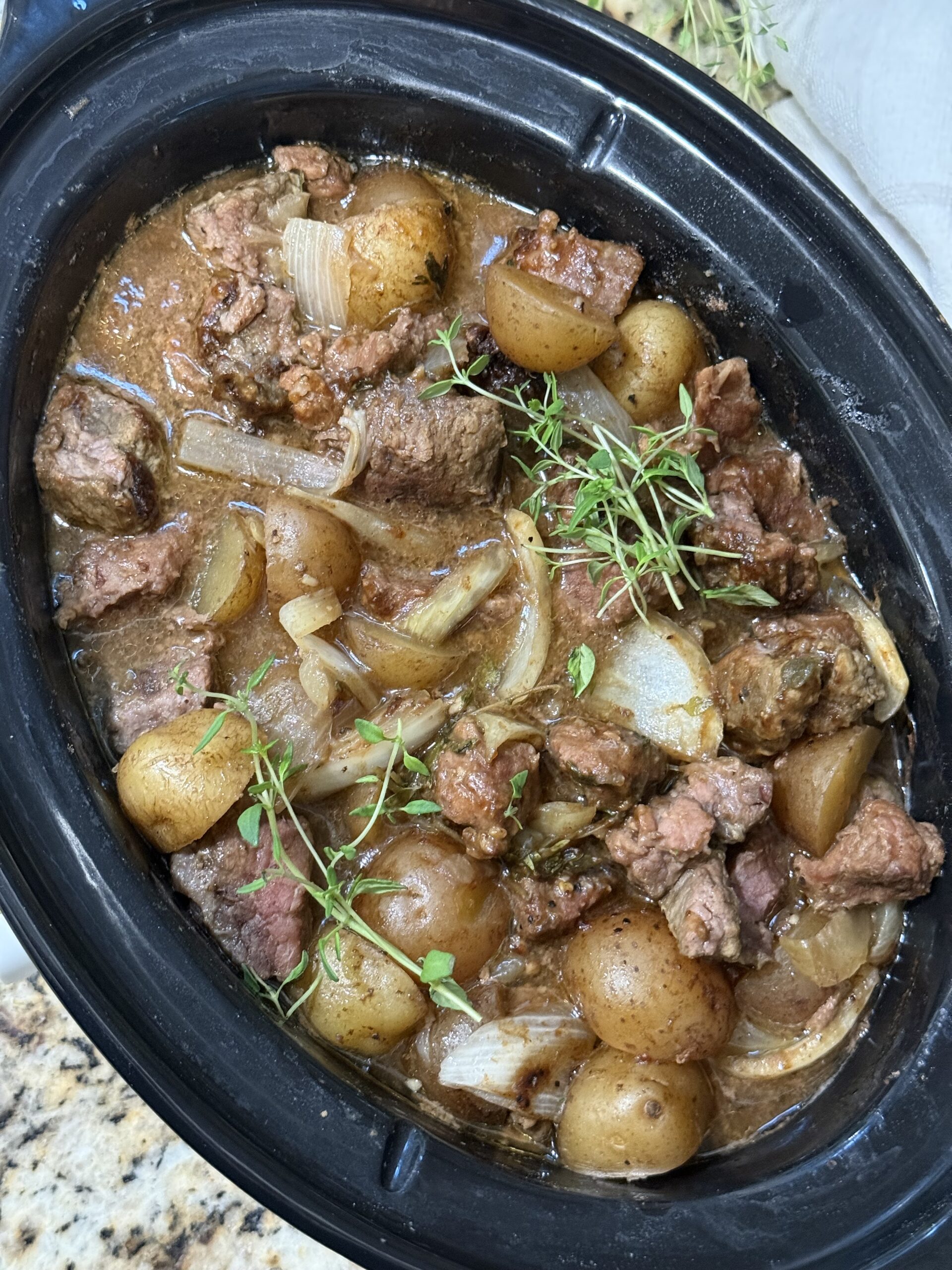 Crockpot steak bites and baby potatoes coated in savory beef gravy and garnished with fresh thyme