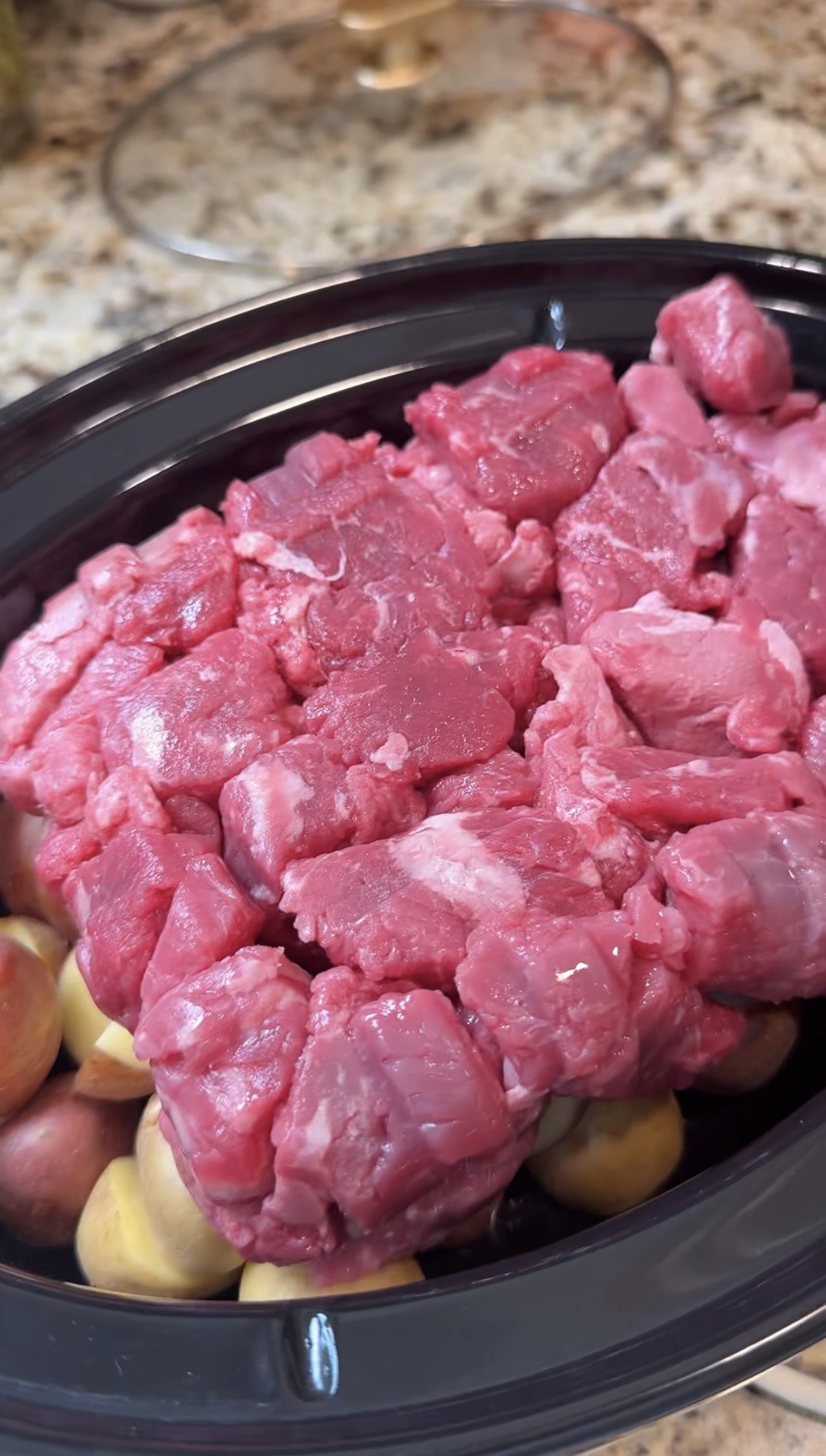 Raw steak bites and halved baby potatoes in a slow cooker