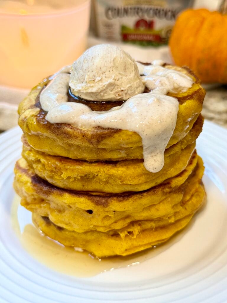 Fluffy pumpkin cinnamon roll pancakes topped with cinnamon swirl and creamy Greek yogurt glaze