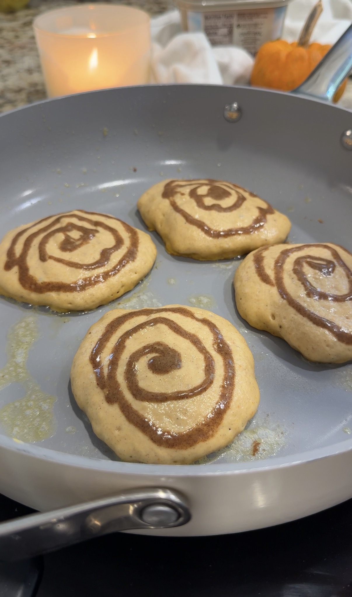 Pumpkin pancakes cooking in a nonstick skillet with cinnamon swirls on top
