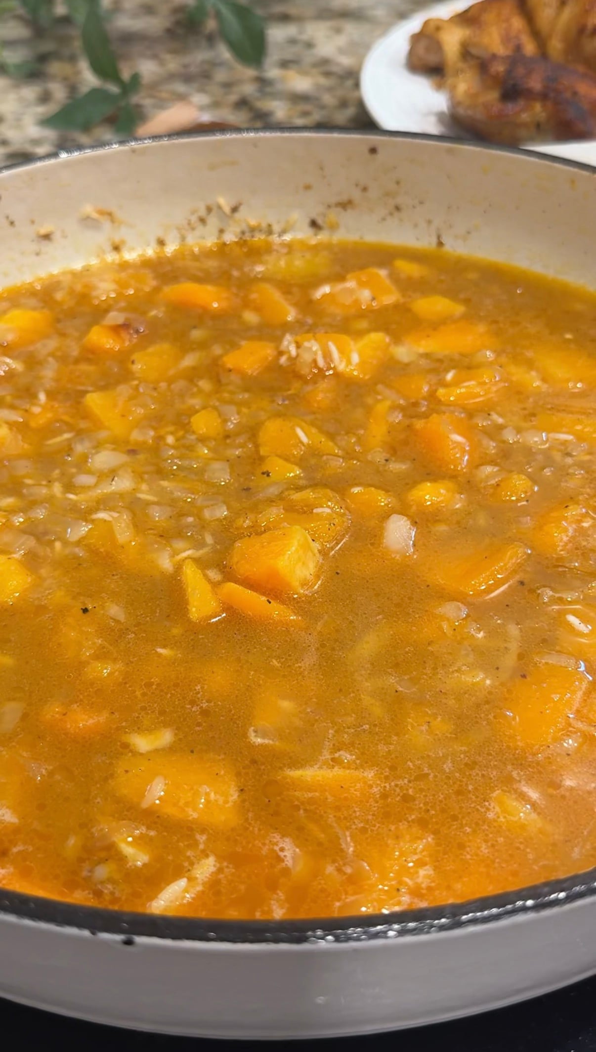 Rice and diced butternut squash simmering in broth with browned chicken thighs