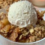 Warm apple crisp with a buttery pecan oat topping served with a scoop of vanilla ice cream