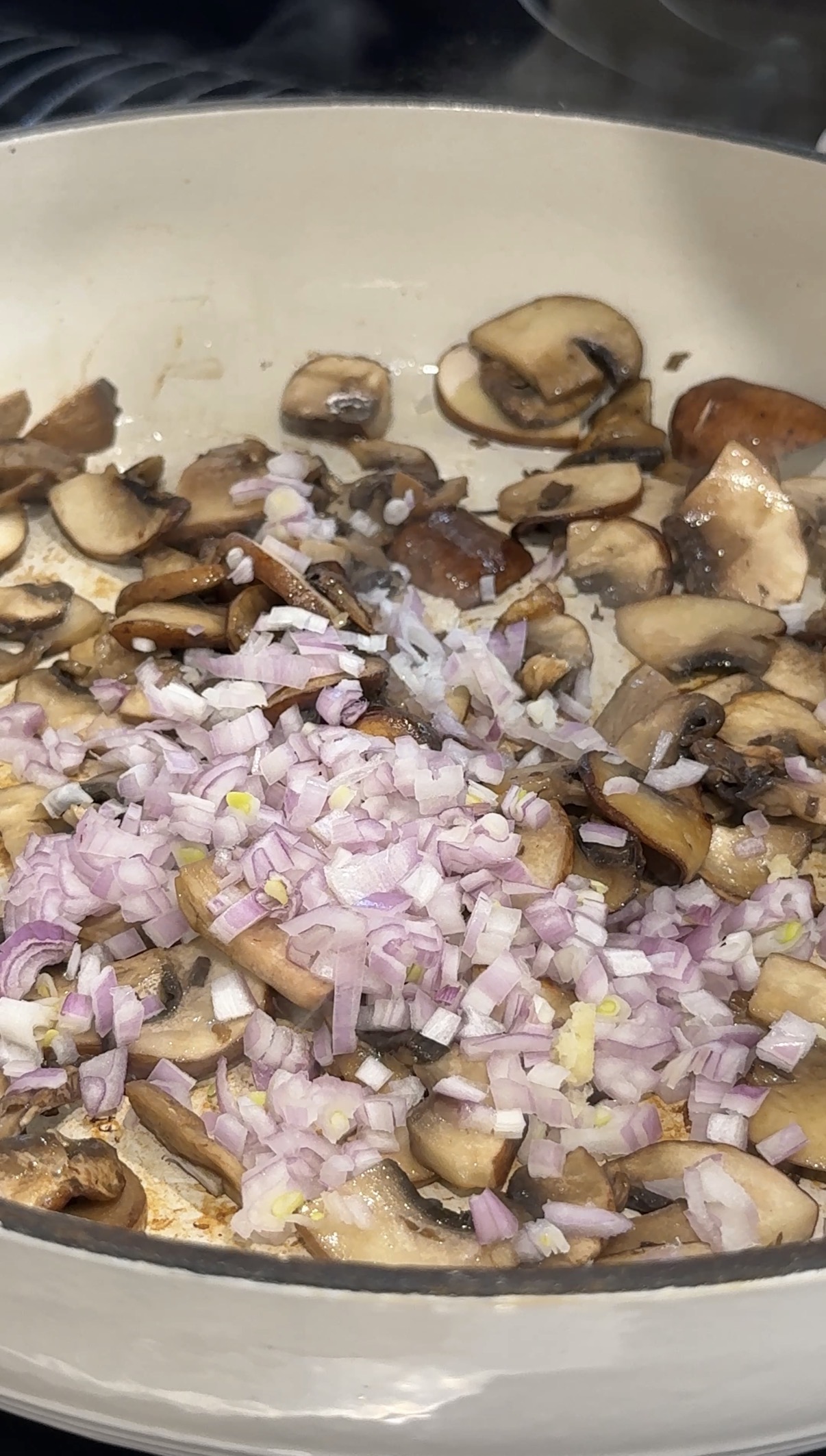 Diced yellow onion and butter added to sautéed mushrooms in a skillet.